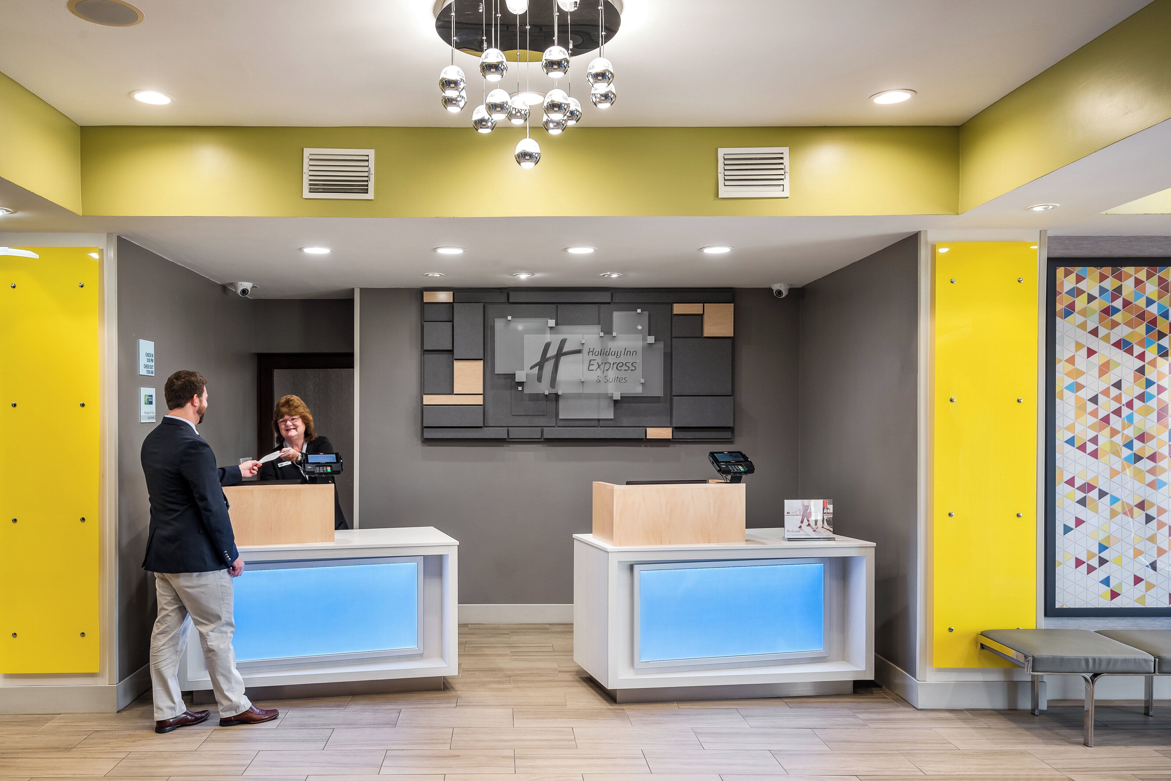 A hotel reception area with two reception desks, a modern chandelier, and a wall-mounted sign.