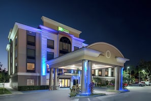 Un hotel Holiday Inn Express con un acceso cubierto, amplias columnas y una fachada bien iluminada.