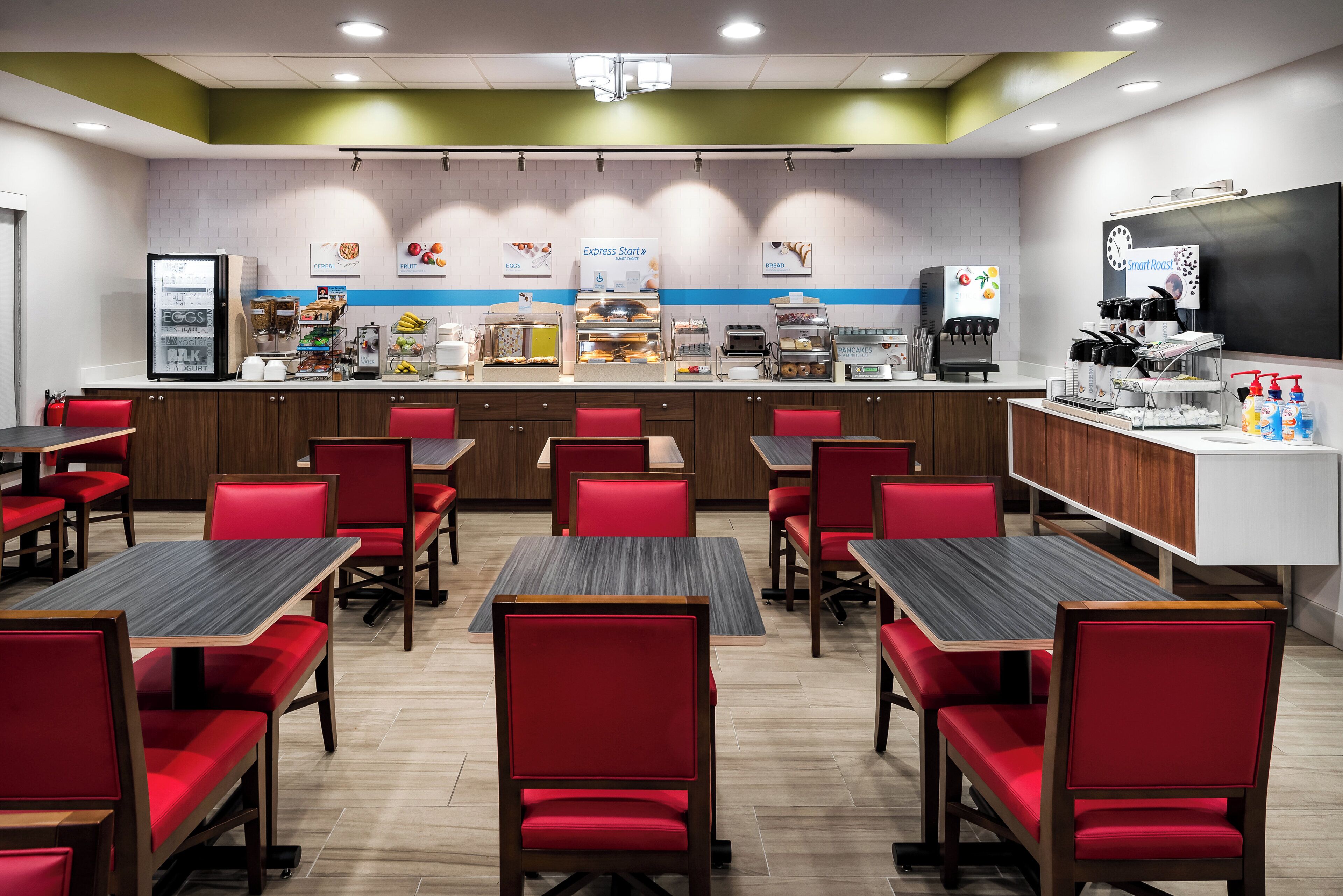 A restaurant with red chairs and tables, a counter with food and drink options, and a coffee machine.