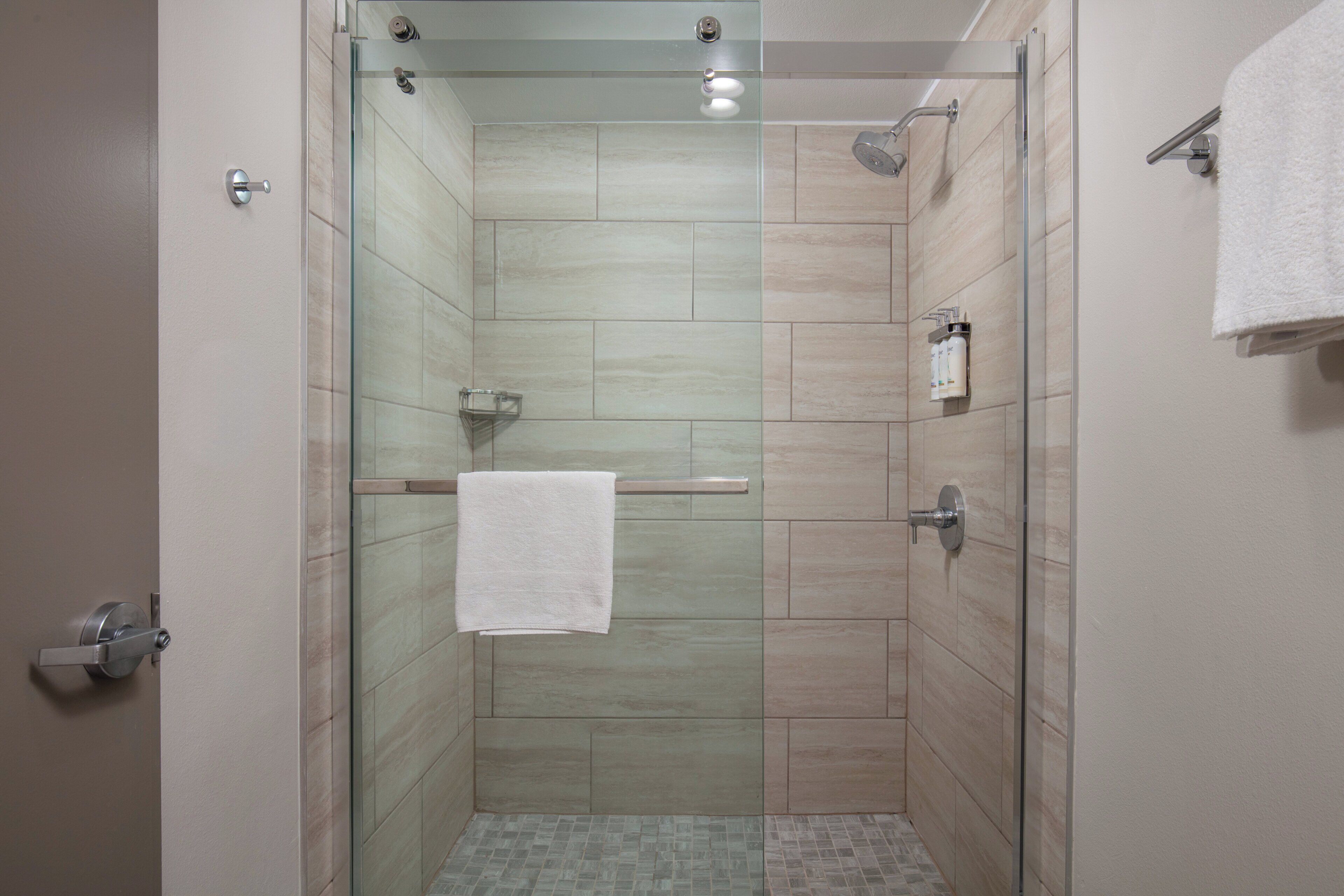 Une douche fermée par des parois en verre, avec une serviette blanche accrochée à la poignée de la porte.