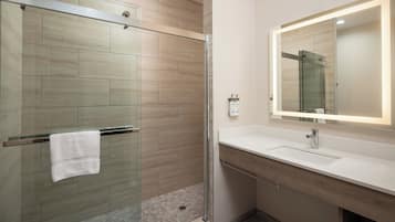A modern bathroom with a glass shower enclosure, a white sink, and a large mirror with integrated lighting.