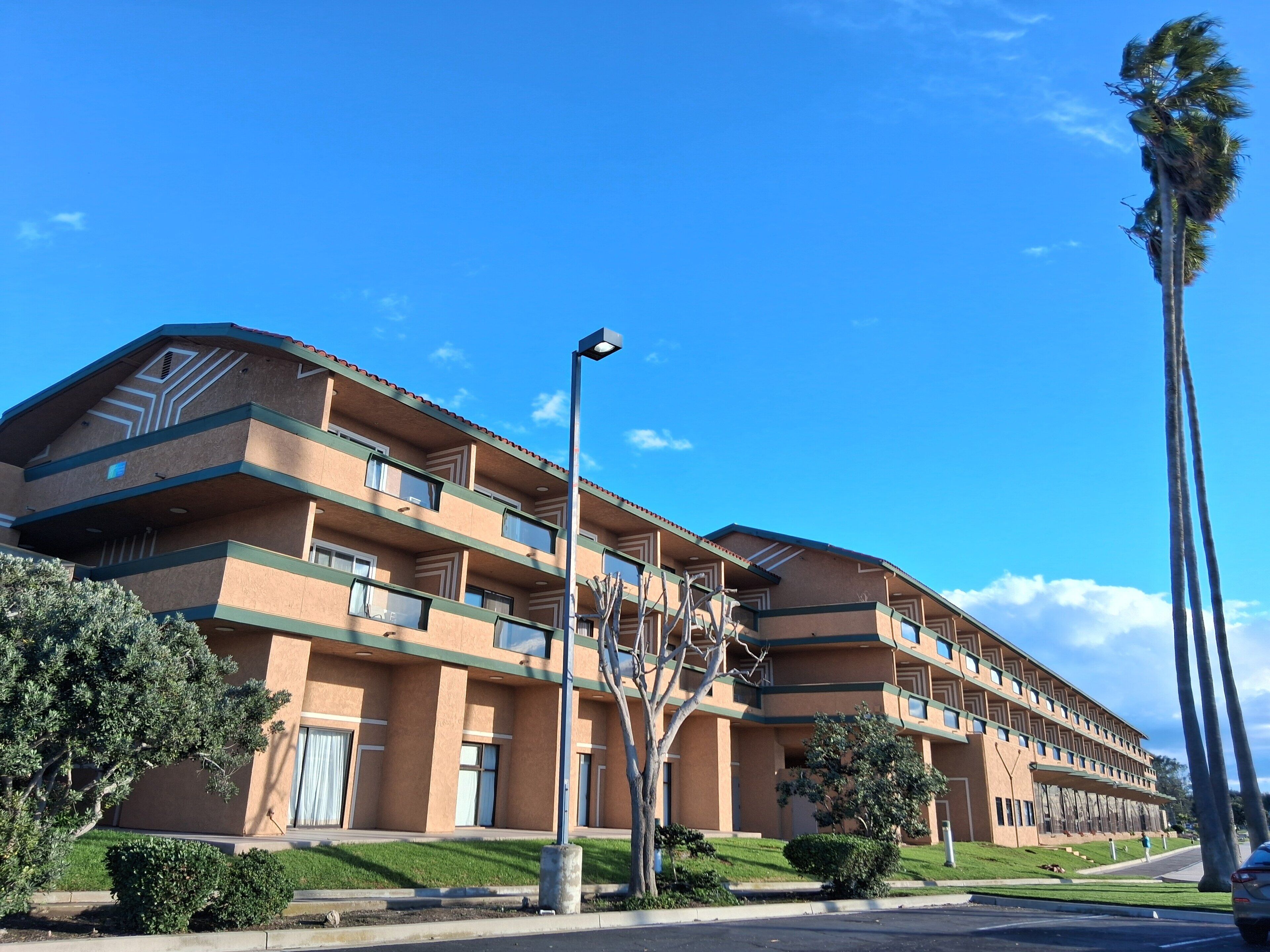 A multi-story hotel with a flat roof, balconies, and a parking lot.