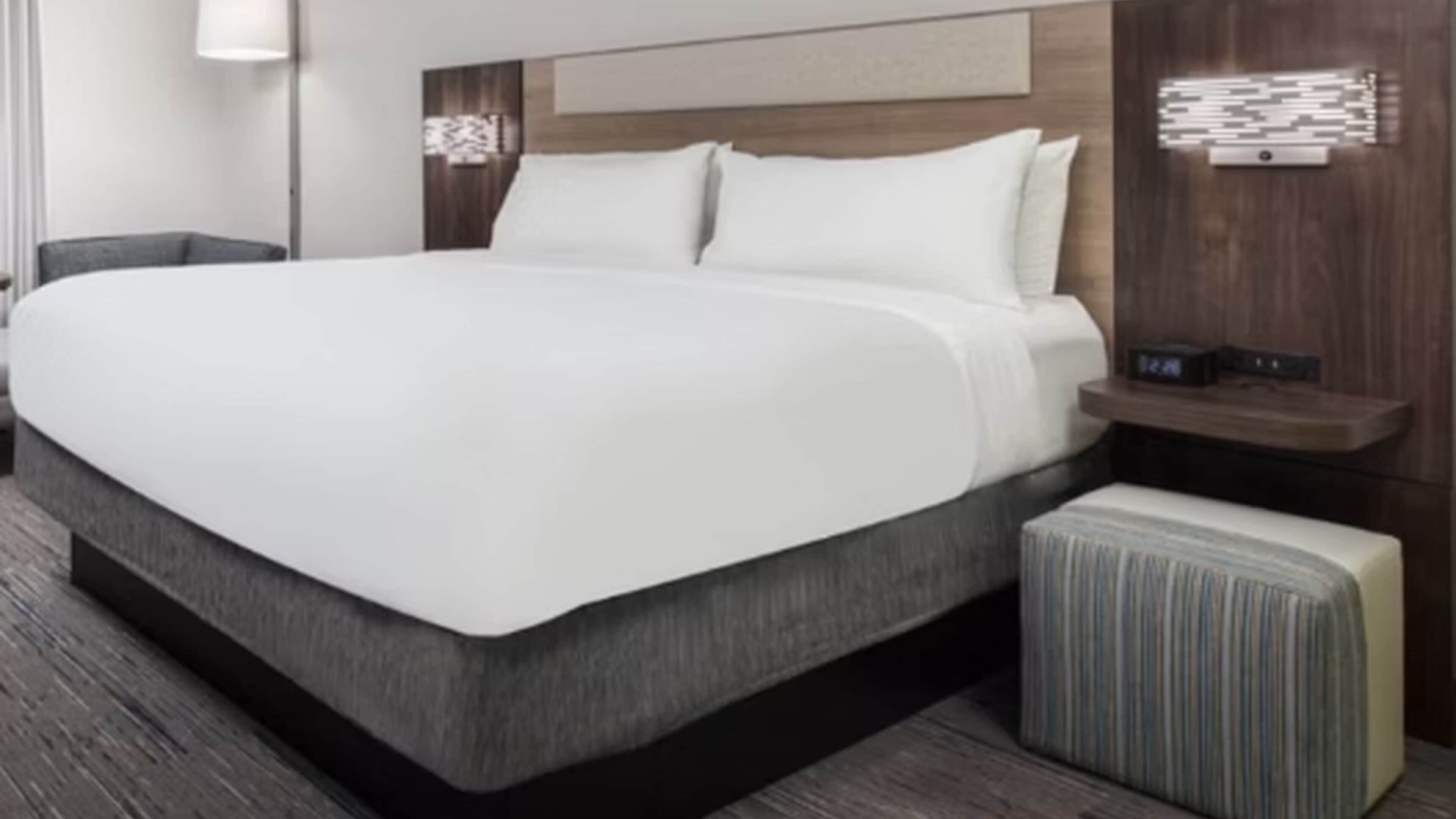 A modern hotel room with a large bed, a bedside table, a nightstand, and a wall-mounted light fixture.