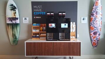 A coffee station with two espresso machines, a shelf with coffee pods, and a surfboard on the wall.