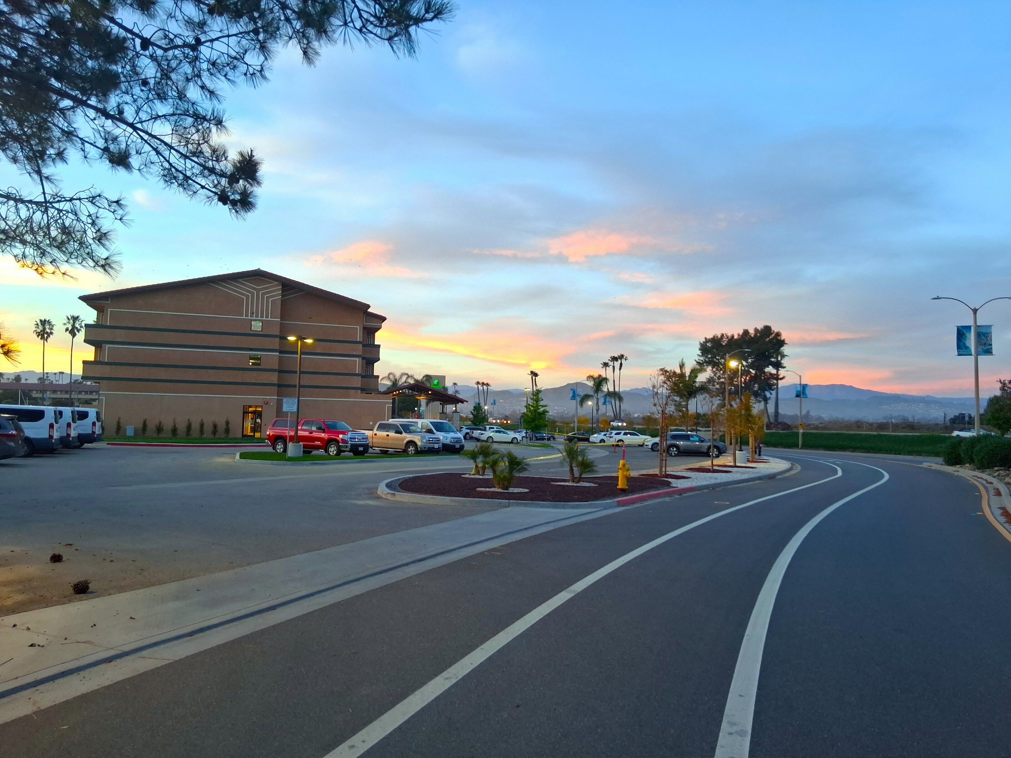 A multi-story hotel with a parking lot, a roundabout, and palm trees.