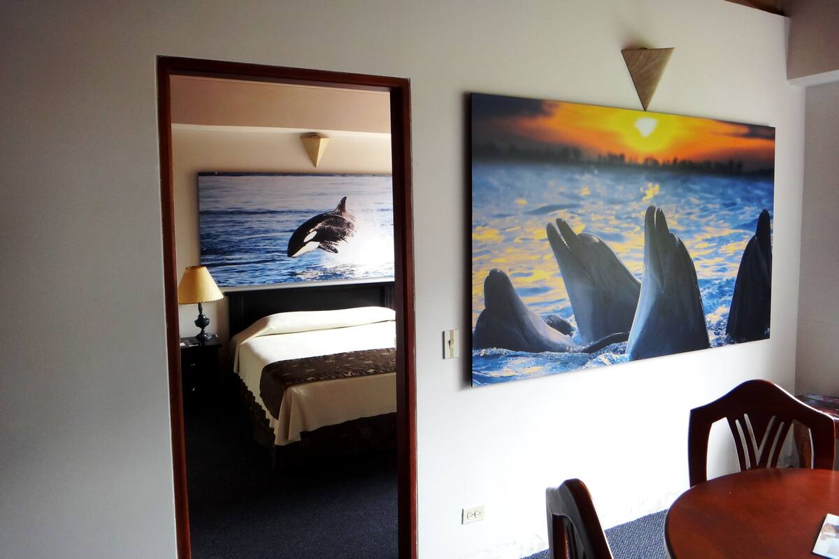 Une pièce comprenant un lit, une table et un mur orné de deux tableaux représentant des animaux marins.