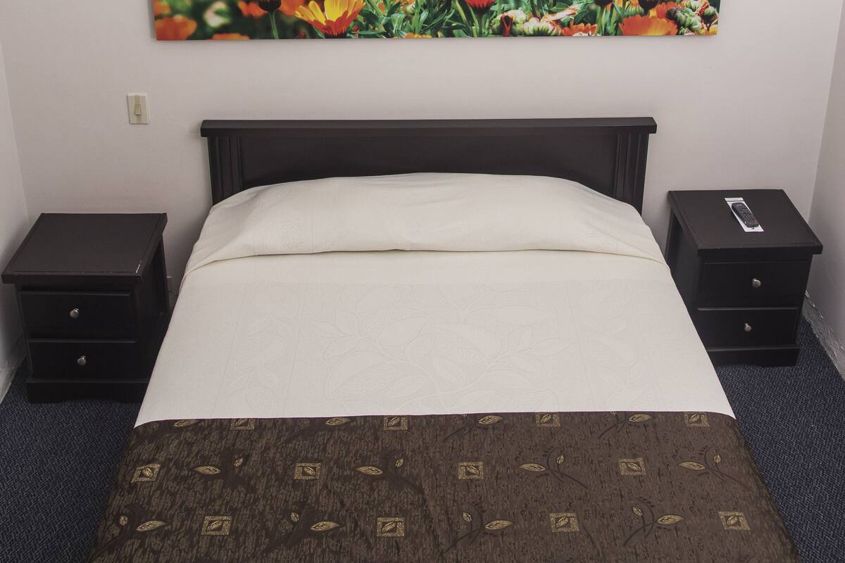 Une chambre d’hôtel avec un lit, deux tables de chevet, un tableau représentant des fleurs accroché au mur et une télécommande posée sur l’une des tables de chevet.