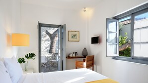 Ein Hotelzimmer mit Bett, Schreibtisch, Stuhl, Pflanze und einem Fenster mit Blick ins Freie.