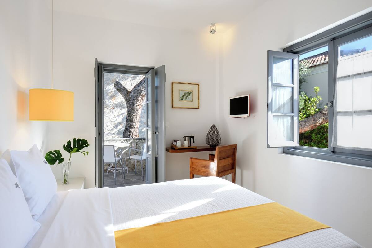 A hotel room with a bed, a desk, a chair, a plant, and a window with a view of the outdoors.