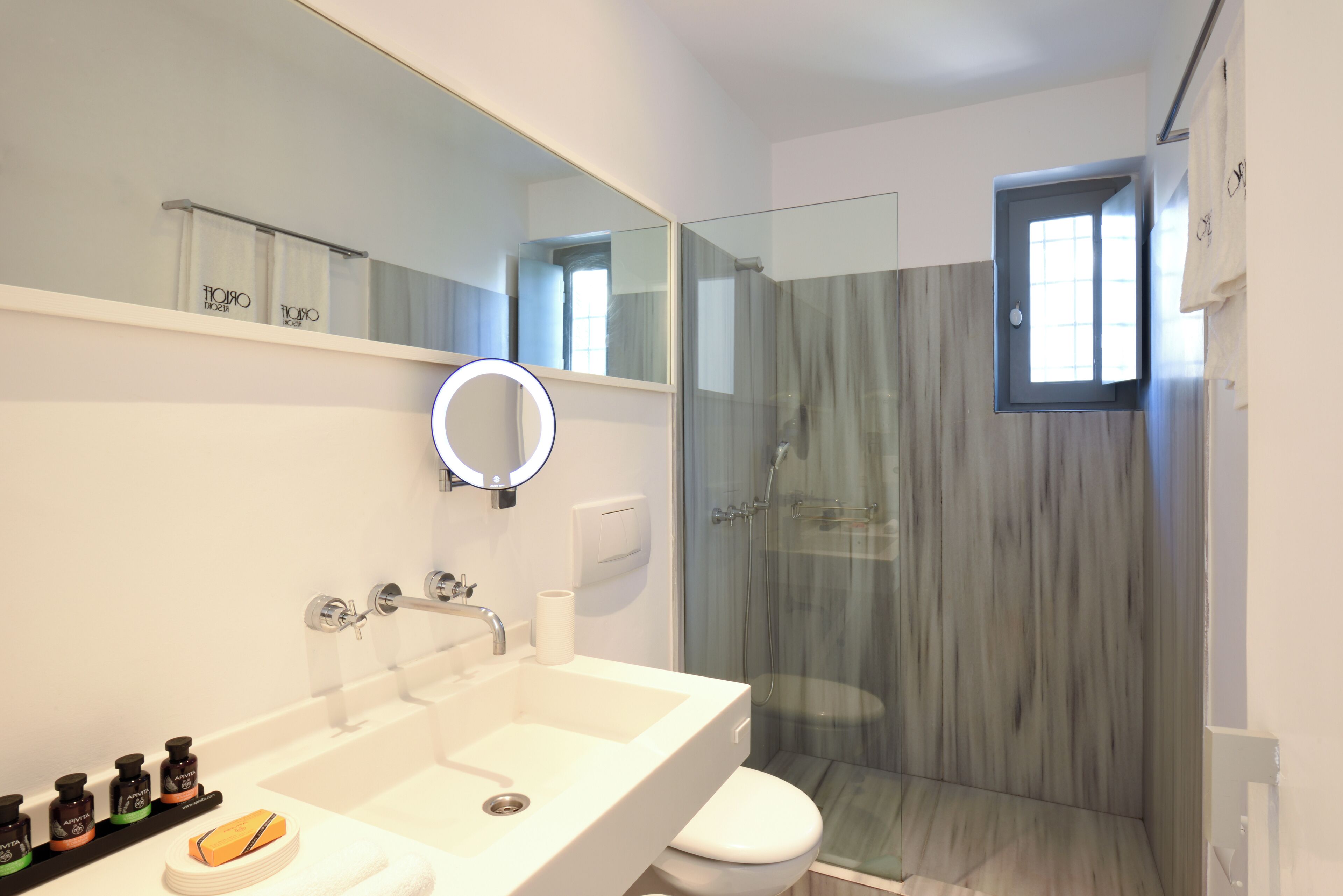 Une salle de bain moderne avec un grand miroir, une douche en verre et un lavabo blanc.