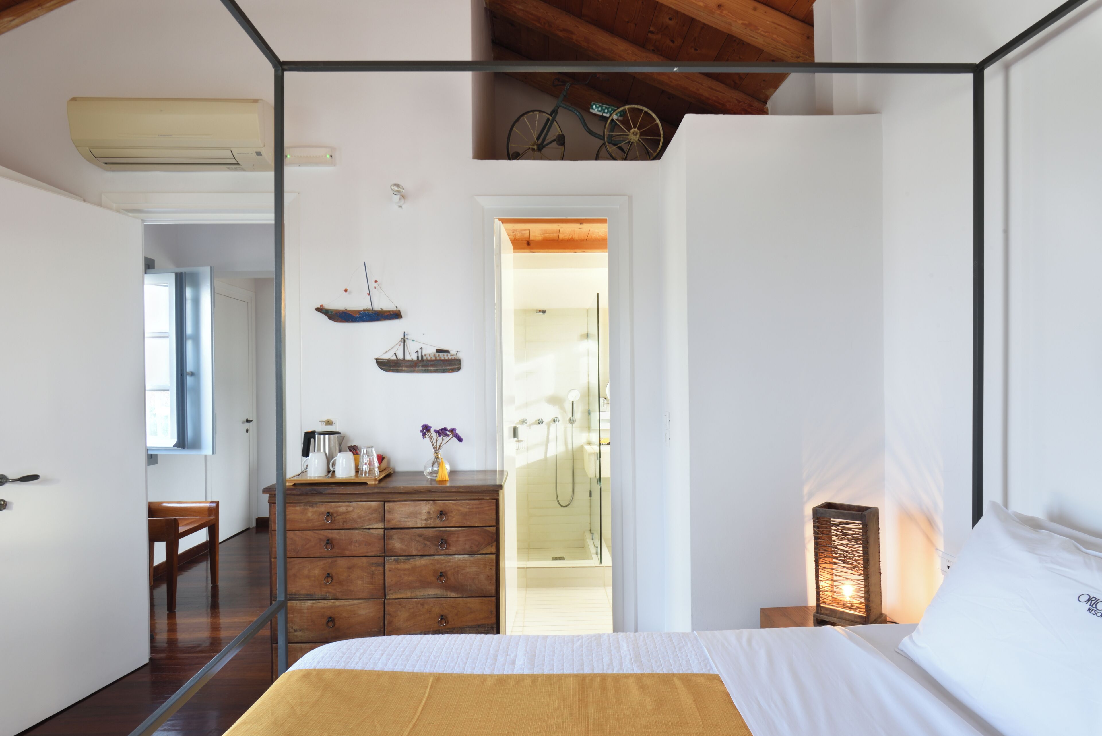 A bedroom with a wooden bed, a dresser, a nightstand with a lamp, and a view of the bathroom.
