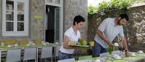 An outdoor dining area with tables set for breakfast, stone walls, and a view of the city.