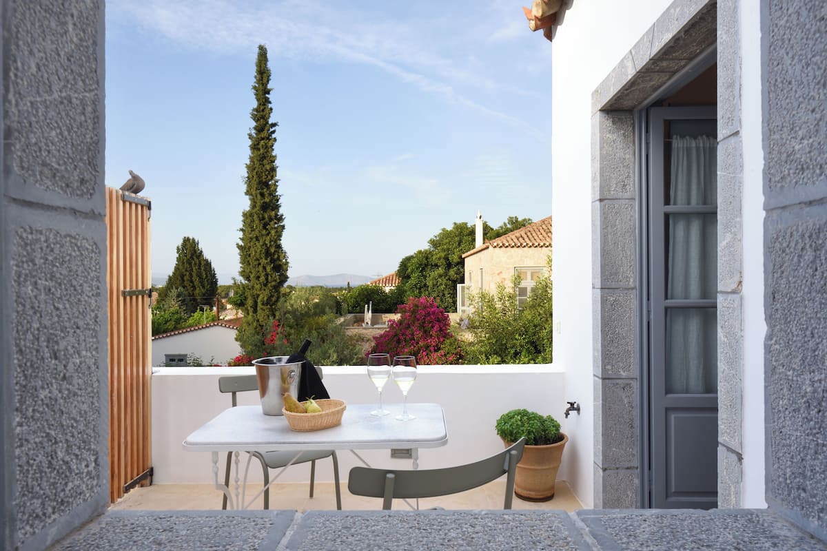 A balcony with a table, two wine glasses, a basket of fruit, and a potted plant.