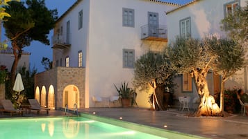Un área junto a la piscina con sillones de descanso, un muro de piedra y un edificio con balcones y ventanas.