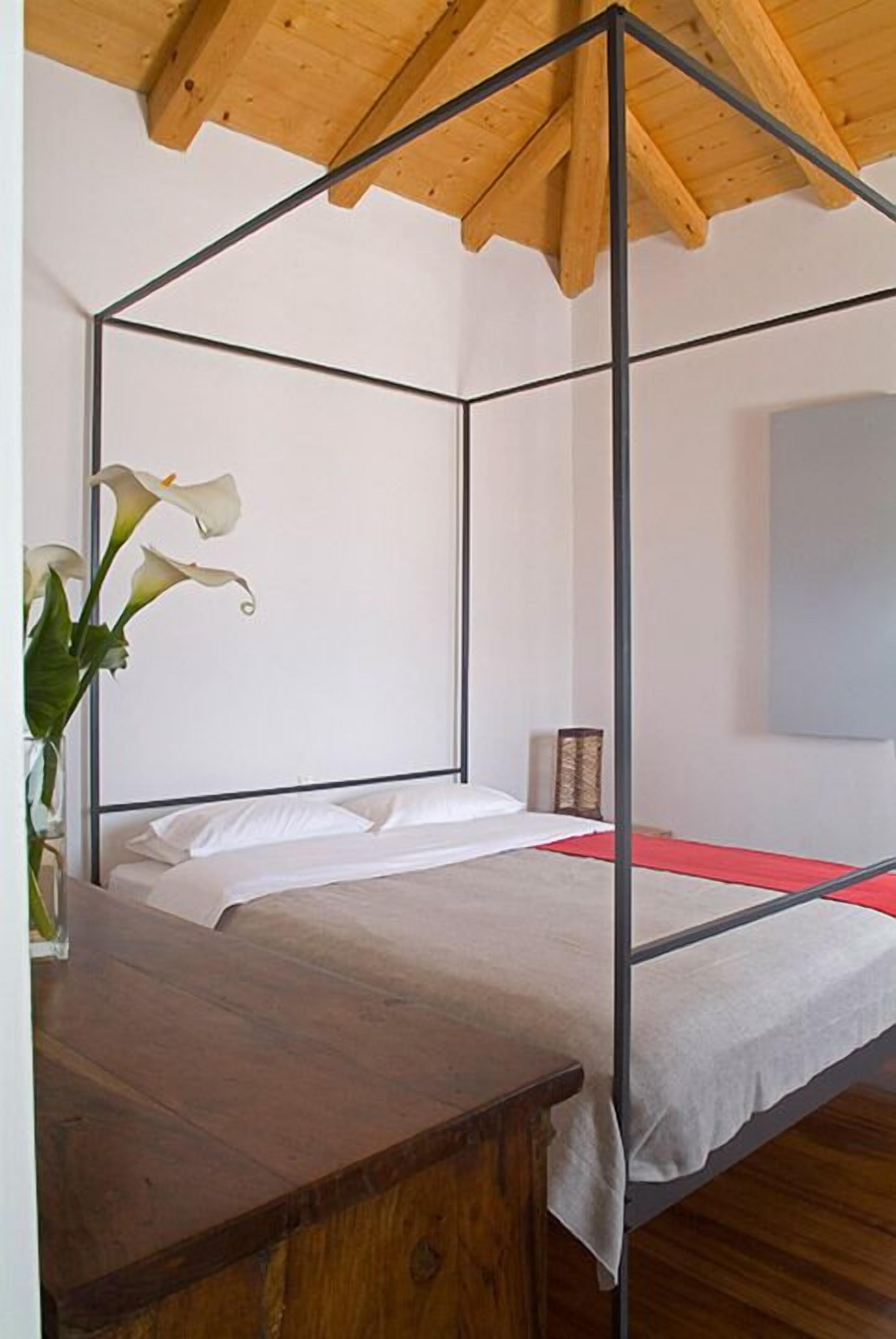 A four-poster bed with a wooden headboard and a vase of white flowers on a wooden nightstand.