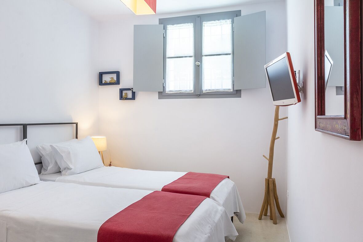A hotel room with two beds, a standing desk, a window with shutters, and a mounted TV.
