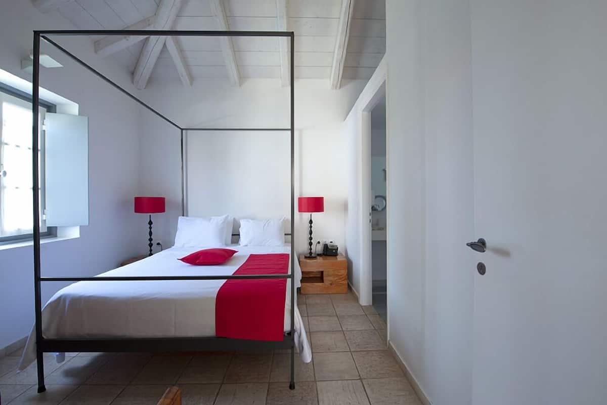 A modern bedroom with a four-poster bed, white bedding, and red accents.