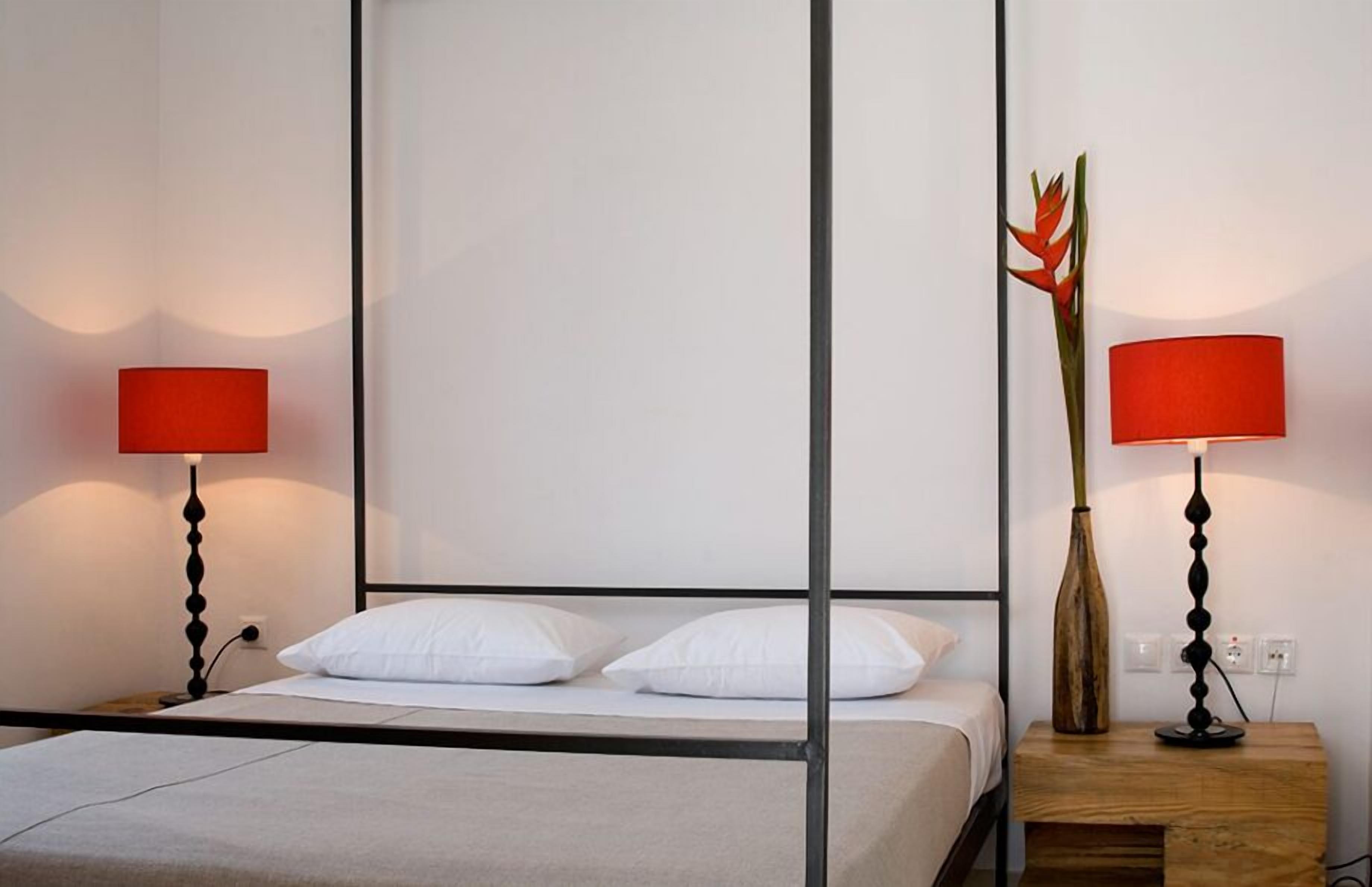 Una habitación de hotel con una cama, dos mesitas de noche y dos lámparas rojas.