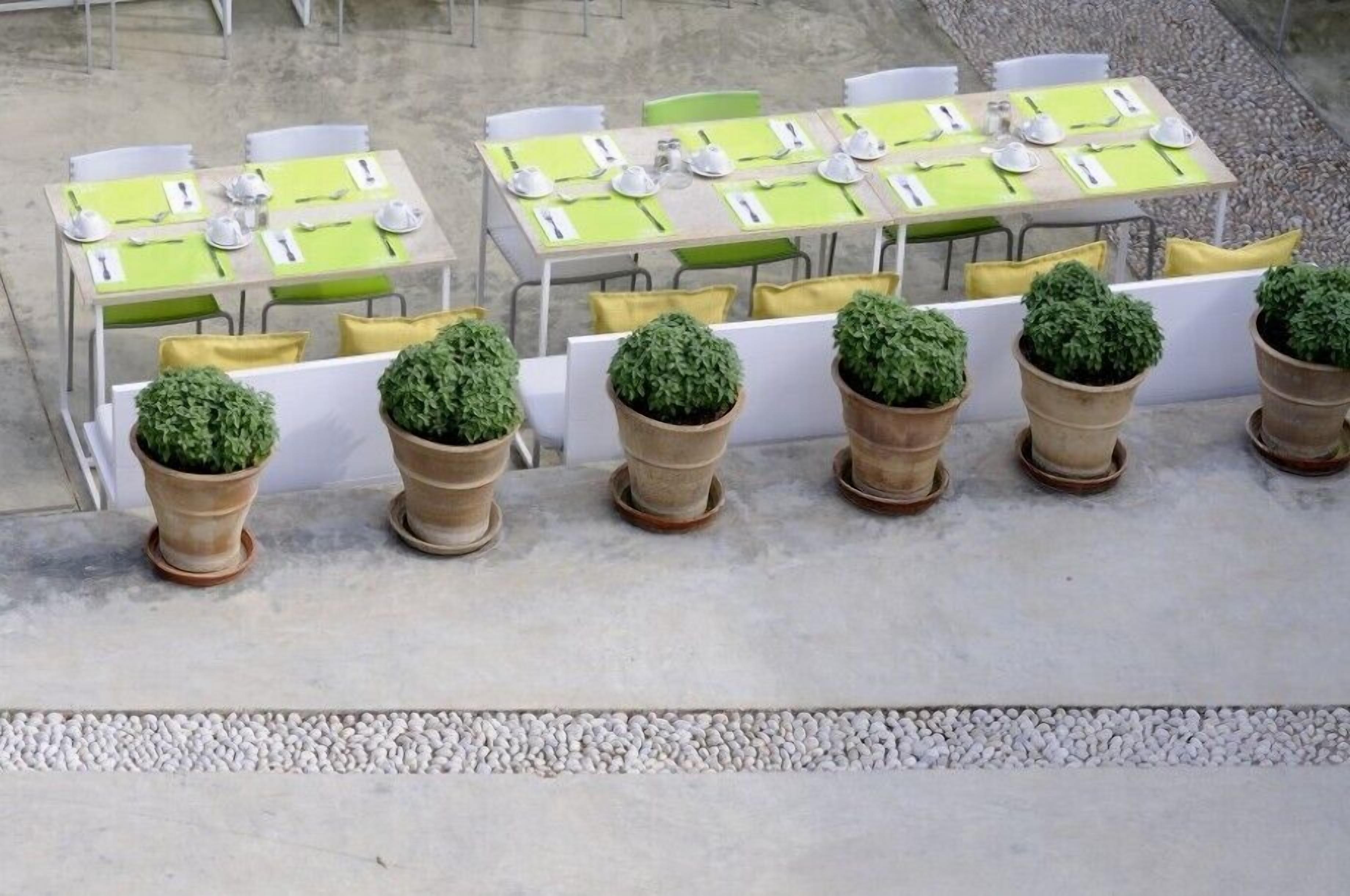 Outdoor dining tables with green tablecloths, white chairs, and potted plants.