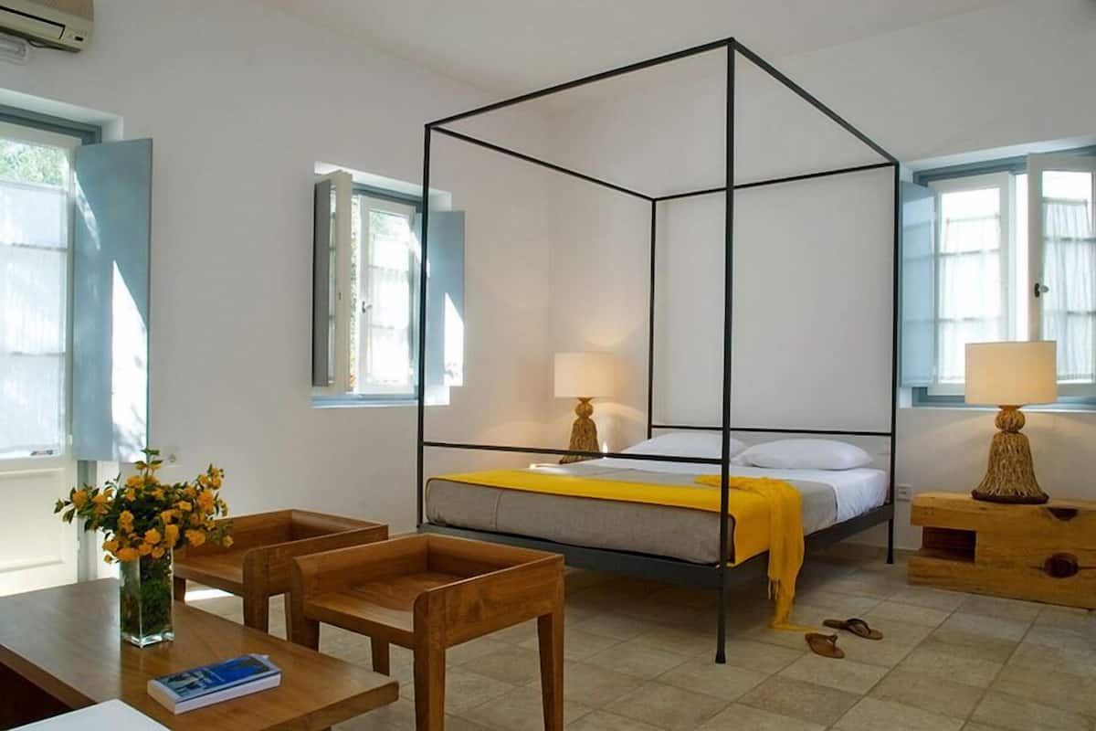 A room with a four-poster bed, wooden furniture, a vase with flowers, and a lamp on a wooden nightstand.