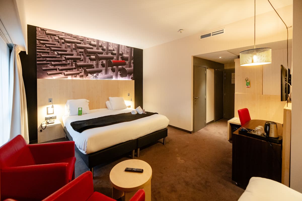 A hotel room with a bed, a desk, a chair, a small table, and a wall with a unique design.