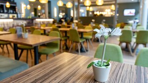 Interior de un restaurante con mesas de madera, sillas verdes y lámparas colgantes.