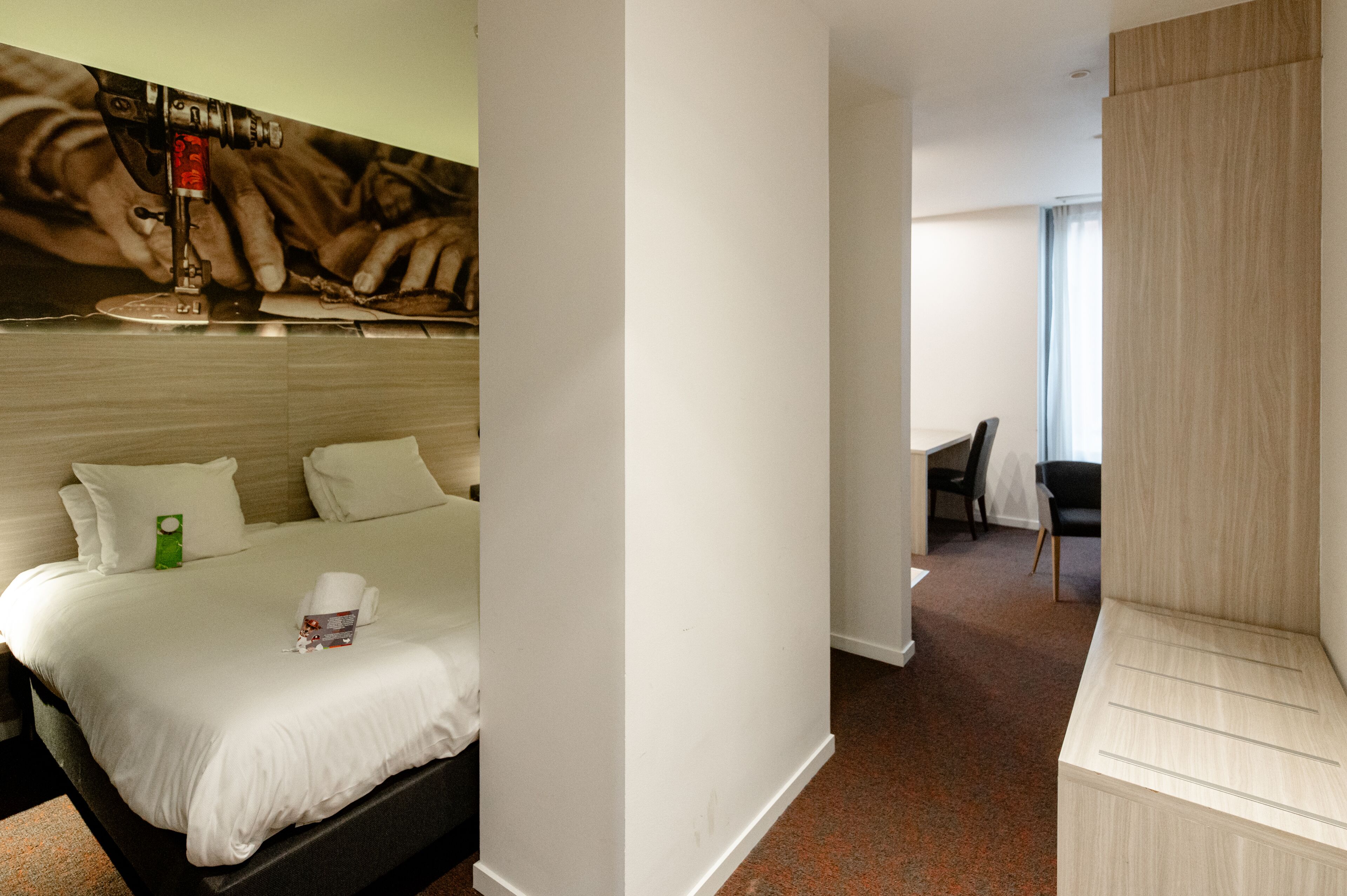 A hotel room with a bed, pillows, a green object on the bed, a chair, and a desk.