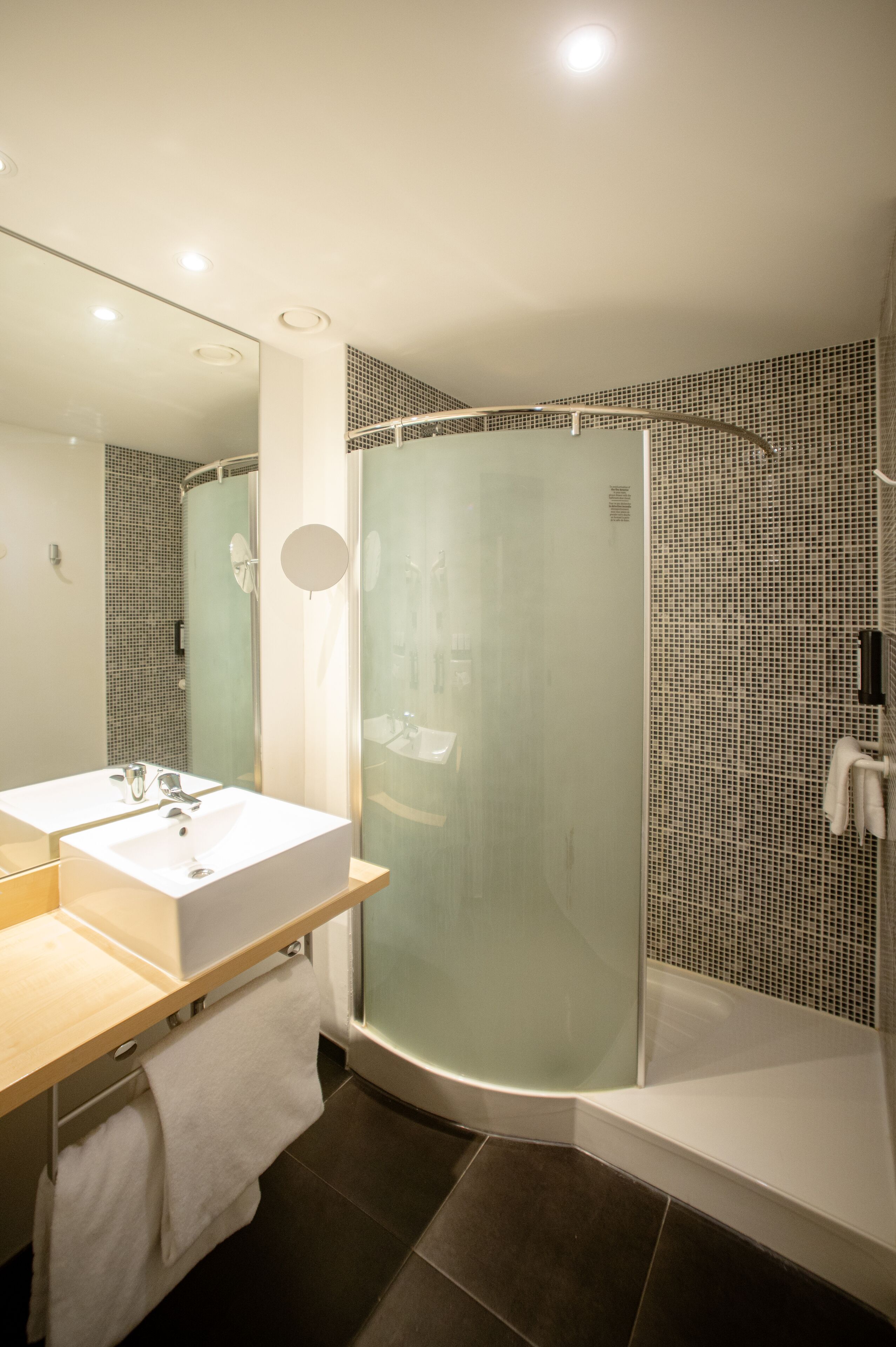 A modern bathroom with a glass-enclosed shower, a large mirror, and a white sink.