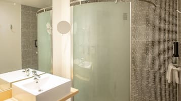 A modern bathroom with a glass-enclosed shower, a large mirror, and a white sink.