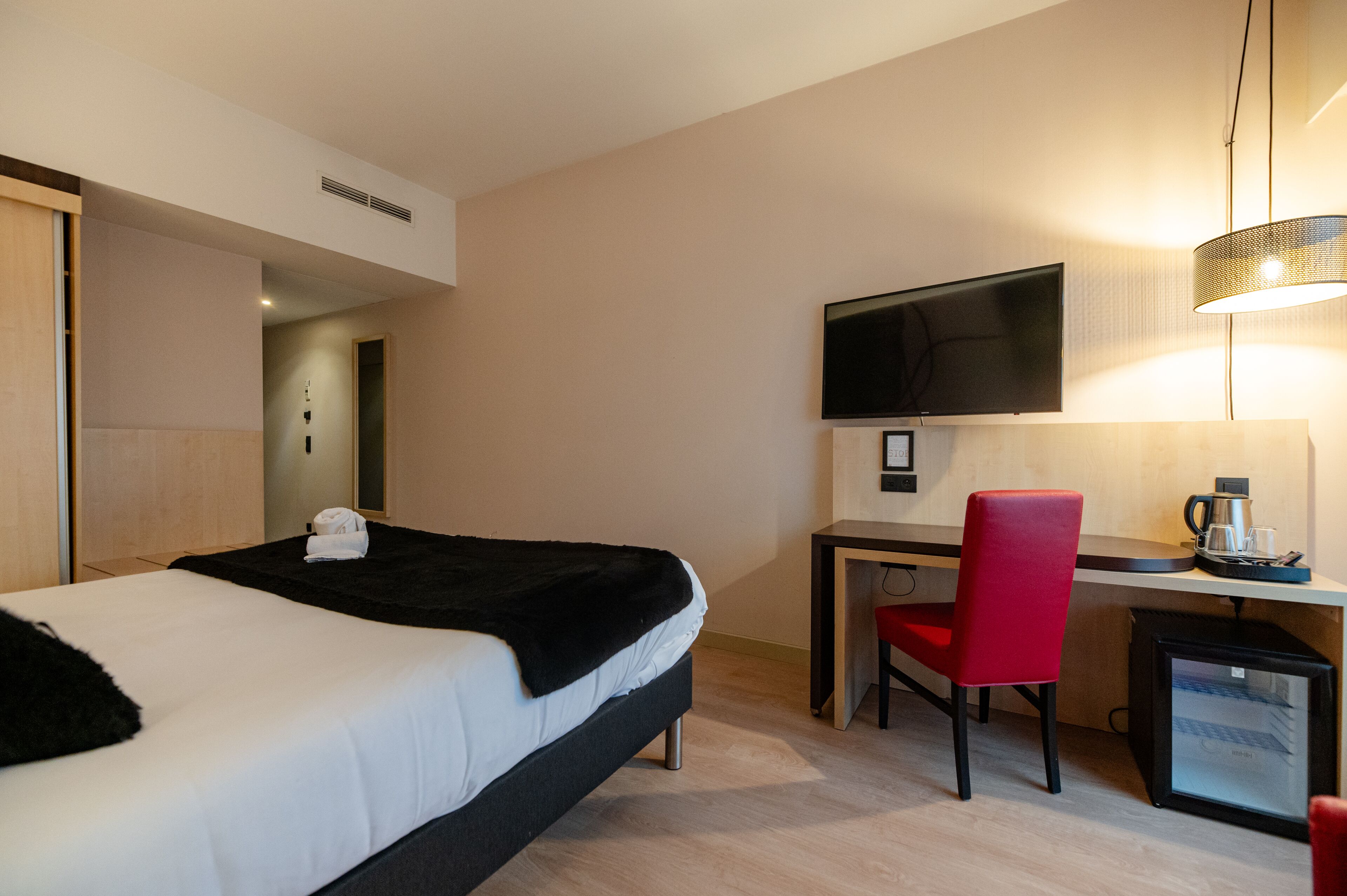 A hotel room with a bed, a desk, a chair, a television, and a coffee maker.