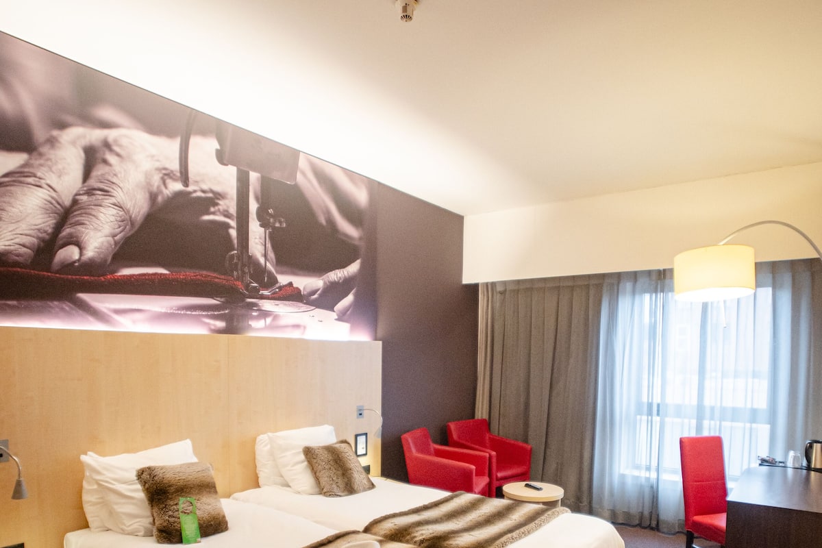 A hotel room with a large bed, two red chairs, a desk, and a large wall-mounted artwork.