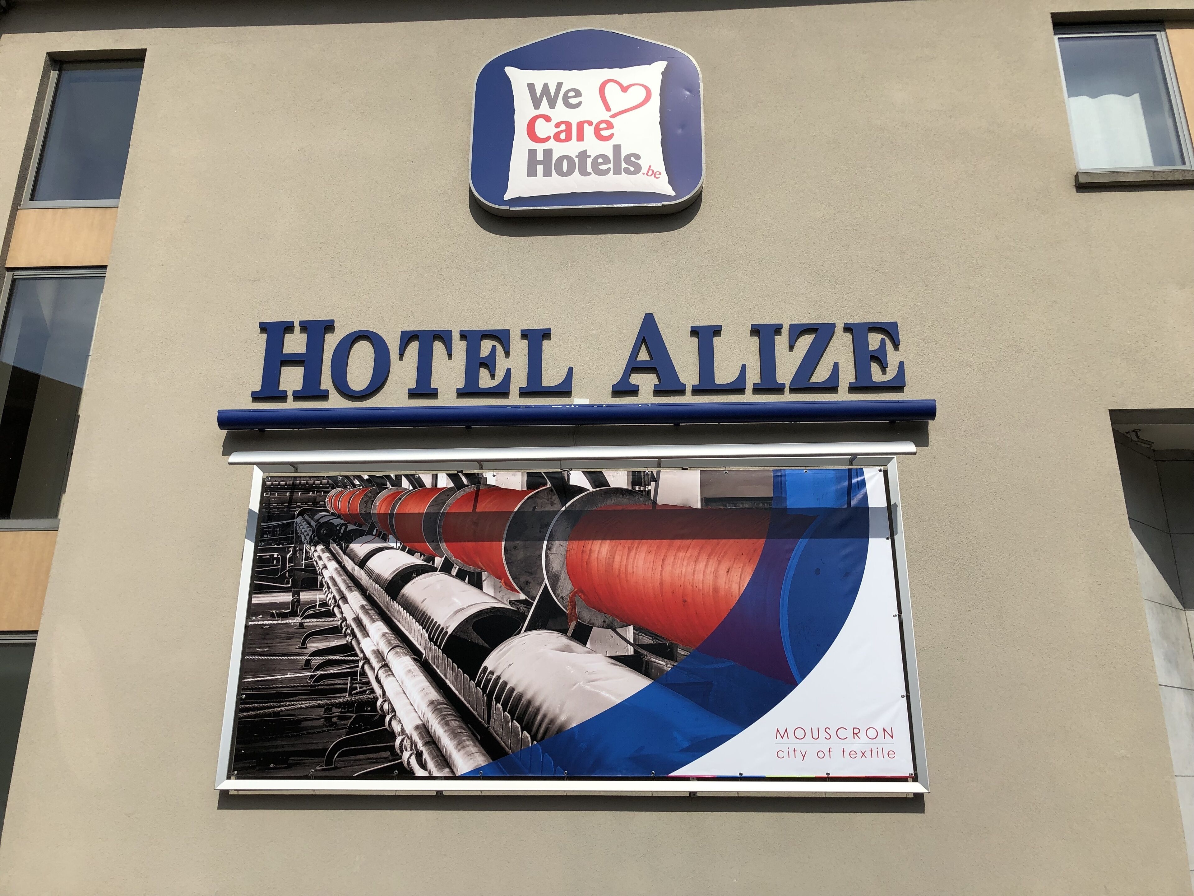 Letrero del Hotel Alize con un cartel que anuncia Mouscron como la ciudad textil.