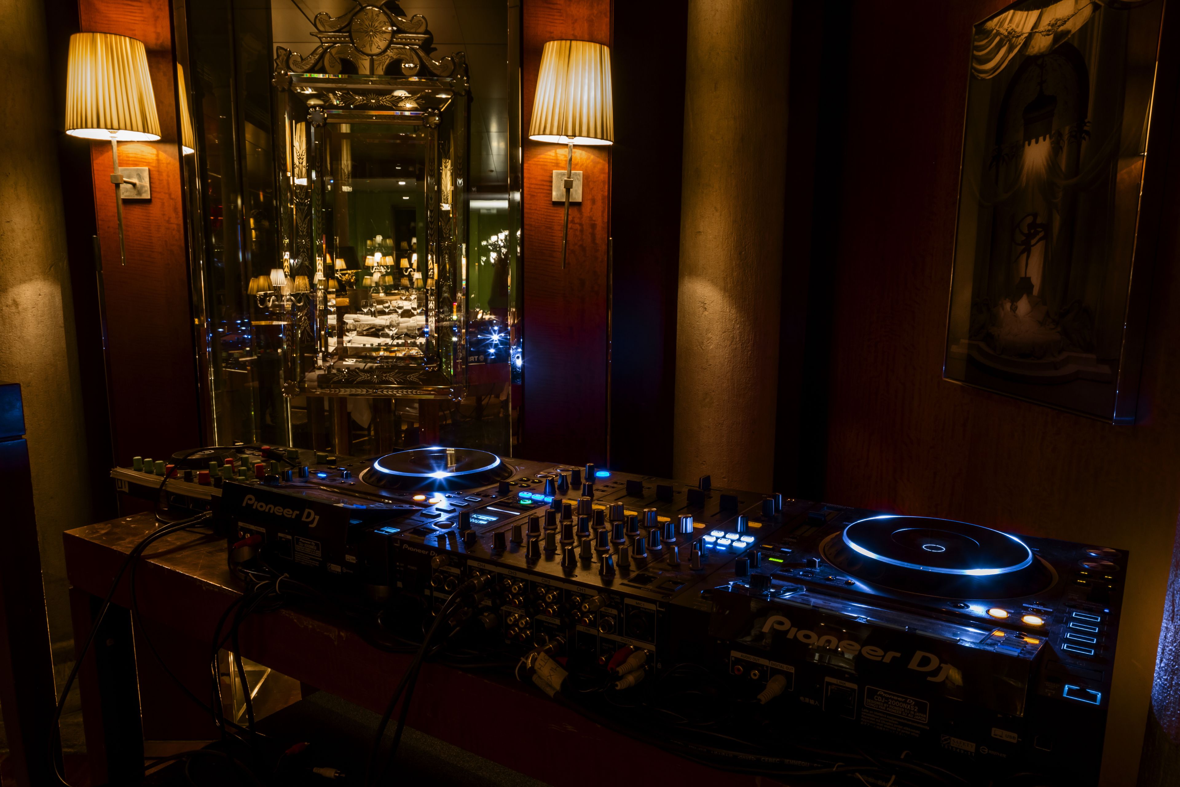A DJ setup with Pioneer DJ equipment, two wall-mounted lamps, and a mirror reflecting the room.