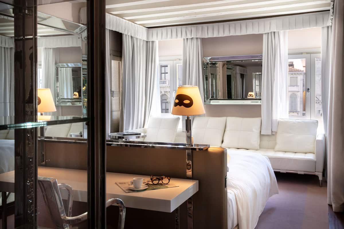 A hotel room with a bed, a desk with a lamp, and a large mirror.