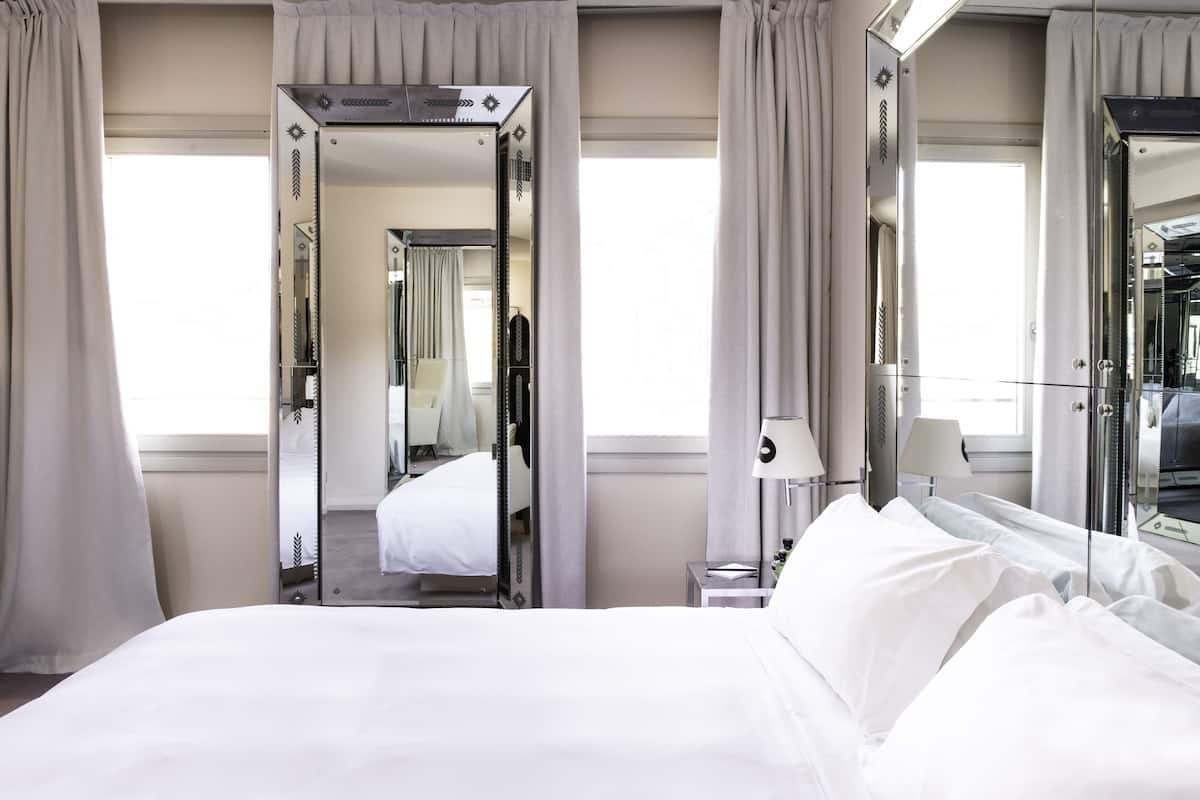 A hotel room with a large bed, a mirror, a bedside table with a lamp, and a view of the hallway.