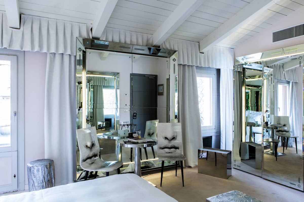 A hotel room with a bed, two chairs, a small table, and a large mirror.