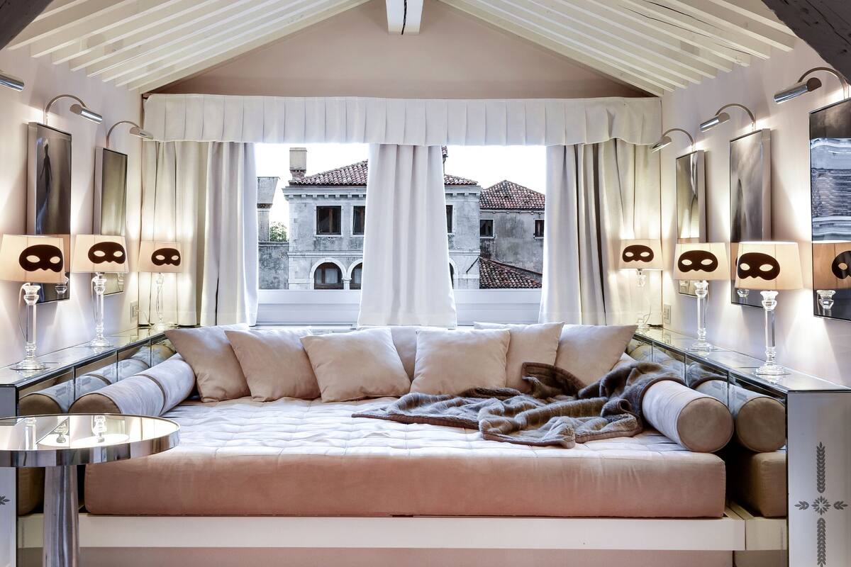 A bedroom with a large bed, a glass bedside table, and a view of a building through the window.