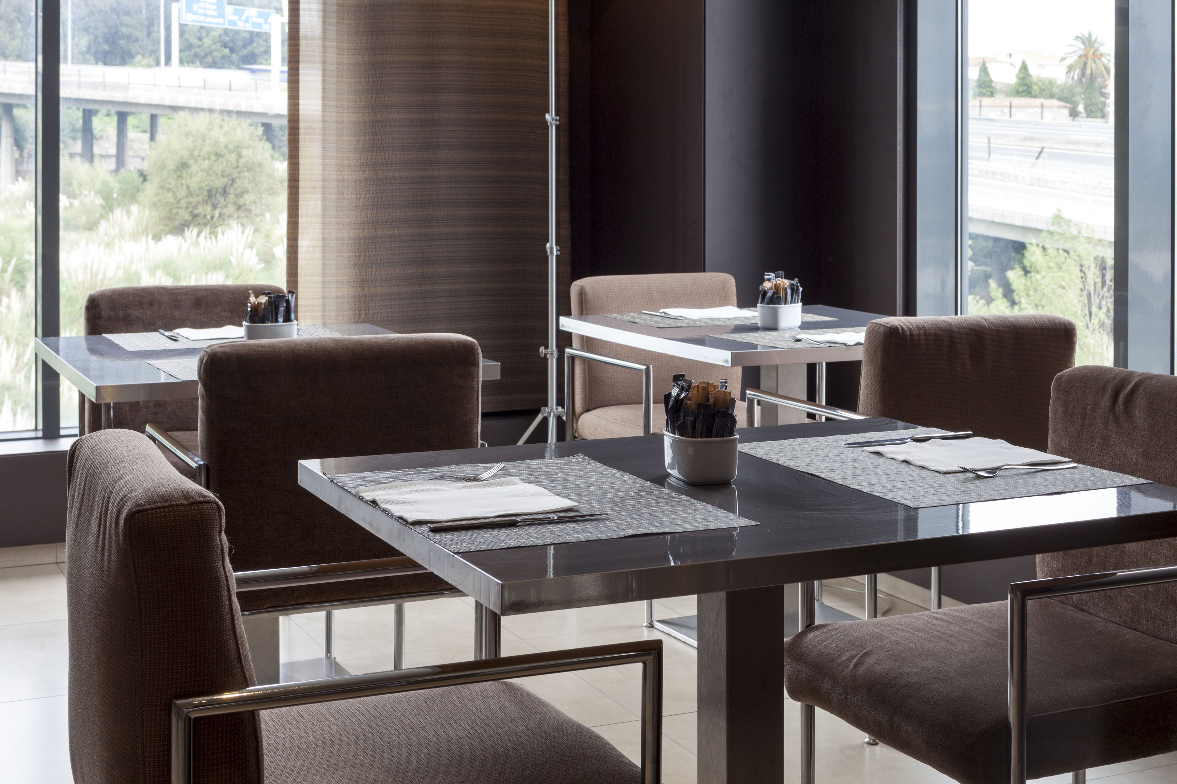 A modern conference room with a glass table, brown upholstered chairs, and a view of a bridge and greenery outside.