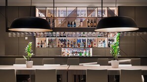 A bar area with a long counter, multiple shelves of bottles, and two large pendant lights. - AC Hotel Porto by Marriott (Porto)