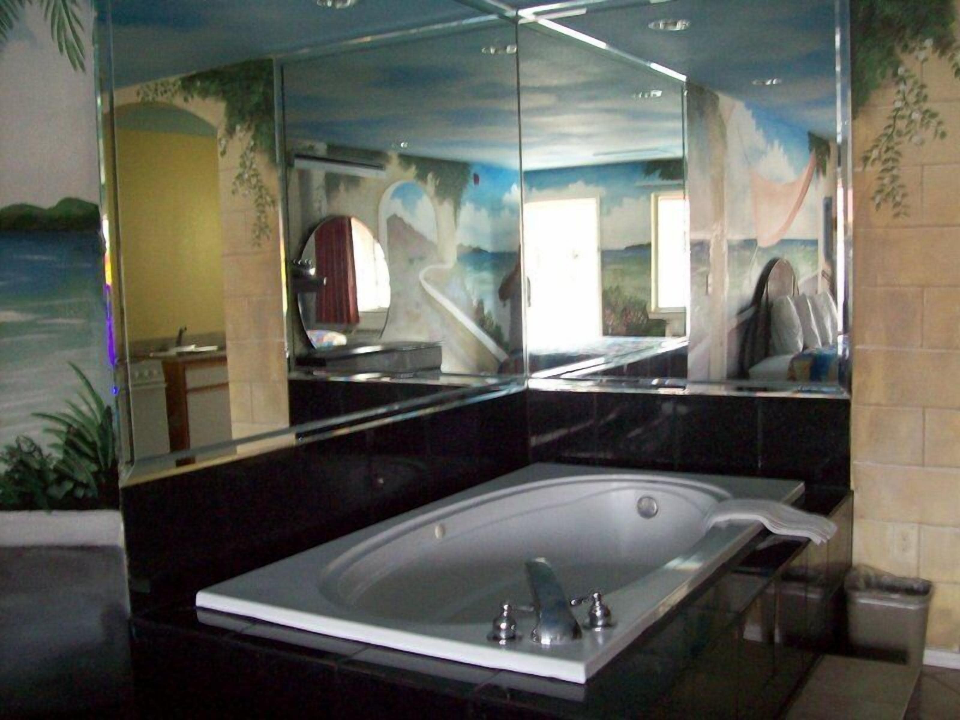 A modern bathroom with a large bathtub, a mirror, and a view of a mountainous landscape.