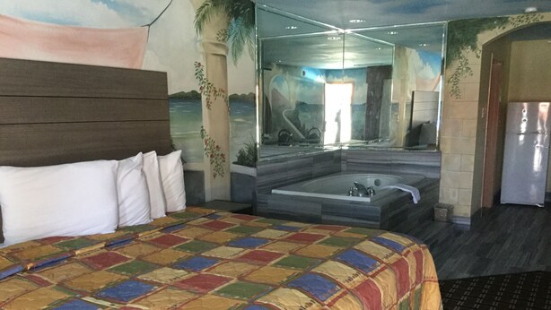 Une chambre d’hôtel avec un grand lit, une baignoire et une vue sur la mer, grâce à une grande fenêtre.