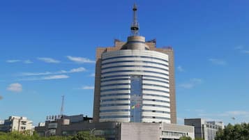 Um edifício alto e cilíndrico com um pináculo central, rodeado por outros edifícios e árvores.