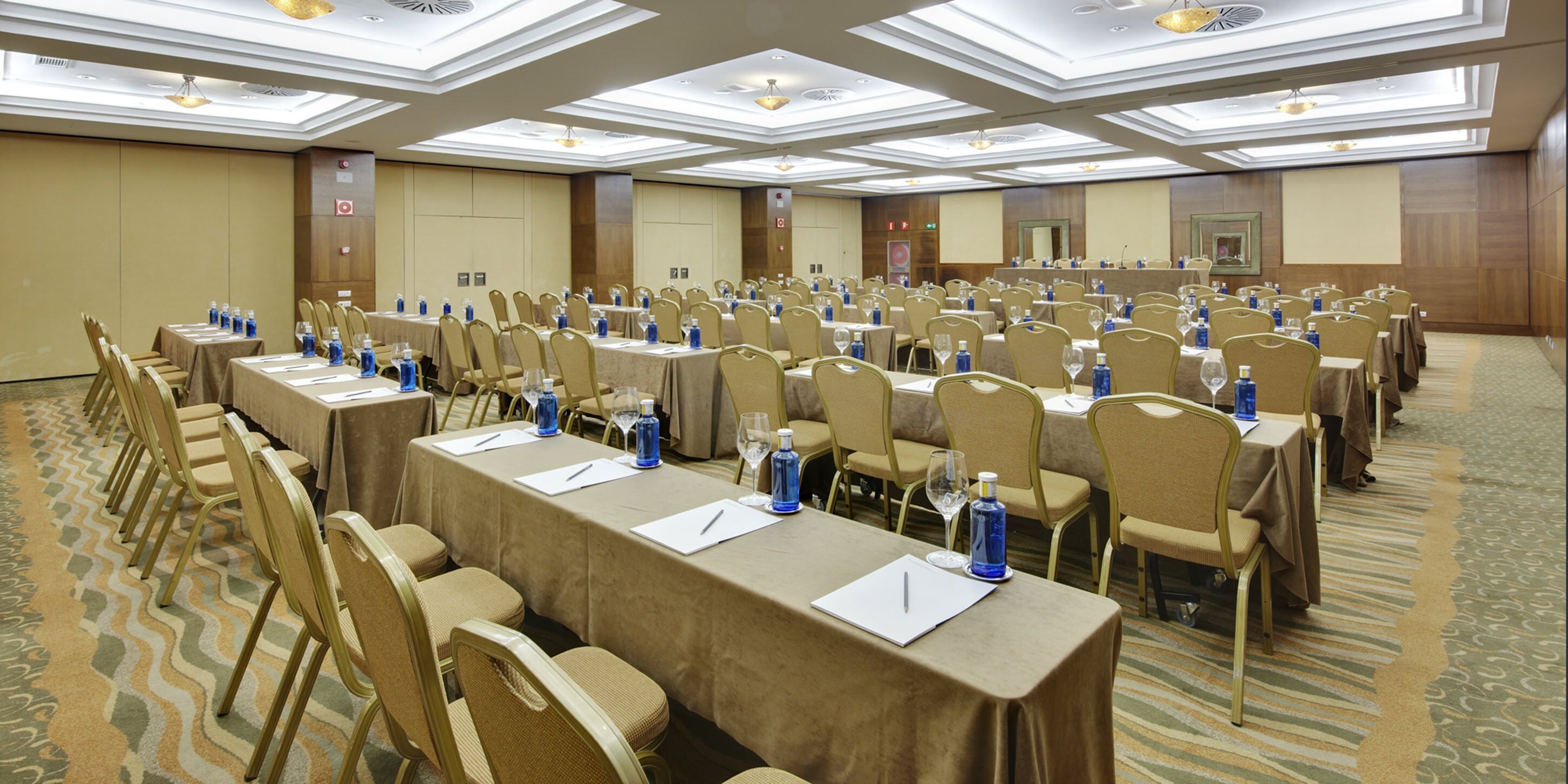 A conference room with rows of tables and chairs, equipped with water bottles and notepads.
