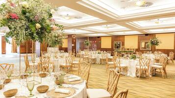 A banquet hall with round tables, wicker chairs, and floral centerpieces.