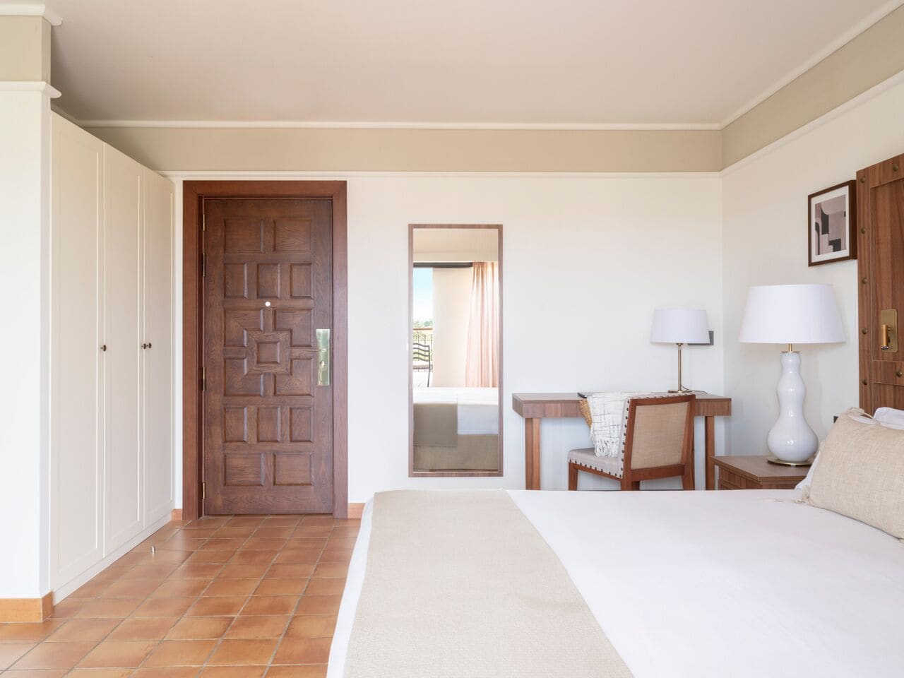 Een hotelkamer met een bed, een bureau, een stoel, een lamp en een kledingkast.