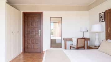 Una habitación de hotel con cama, escritorio, silla, lámpara y armario.