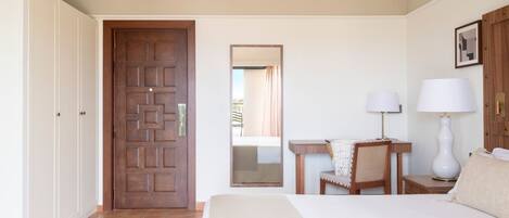 Una habitación de hotel con cama, escritorio, silla, lámpara y armario.