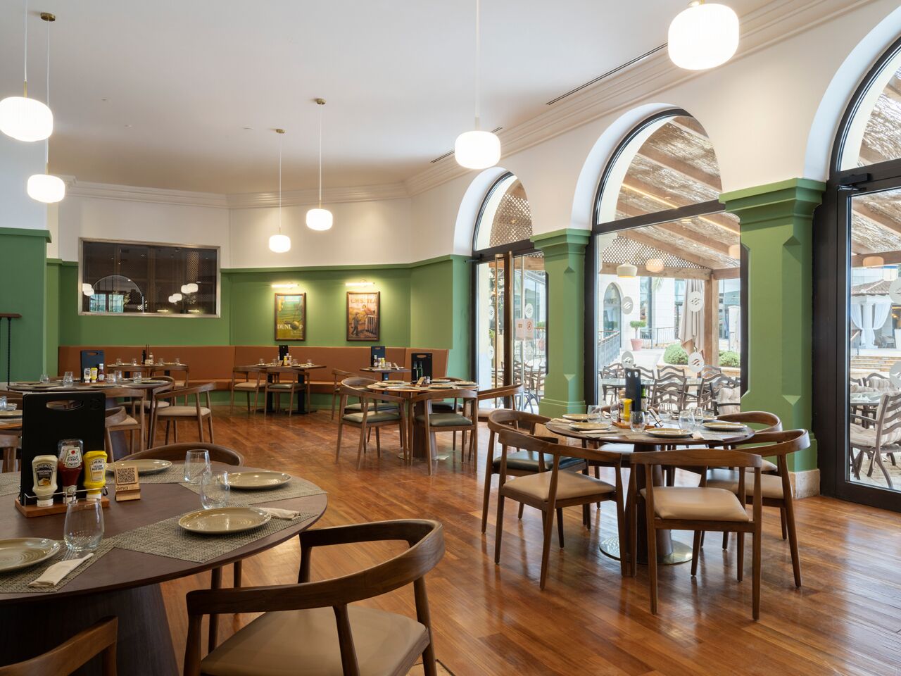 Un restaurante con mesas y sillas de madera, paredes verdes y ventanas amplias.