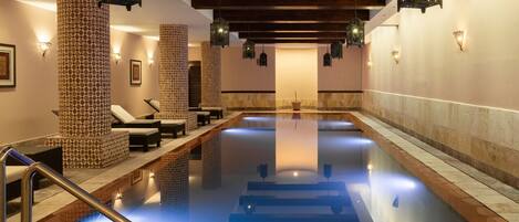 A large indoor swimming pool with lounge chairs and patterned pillars.