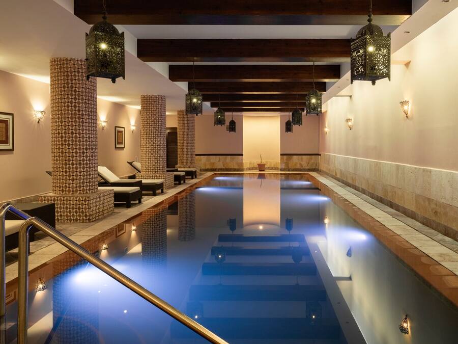 Una gran piscina interior con sillones de descanso y pilares decorativos.